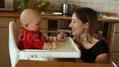 小妈妈带着孩子在厨房。 一个女人坐在高椅上喂婴儿。 <strong>生菜叶</strong>